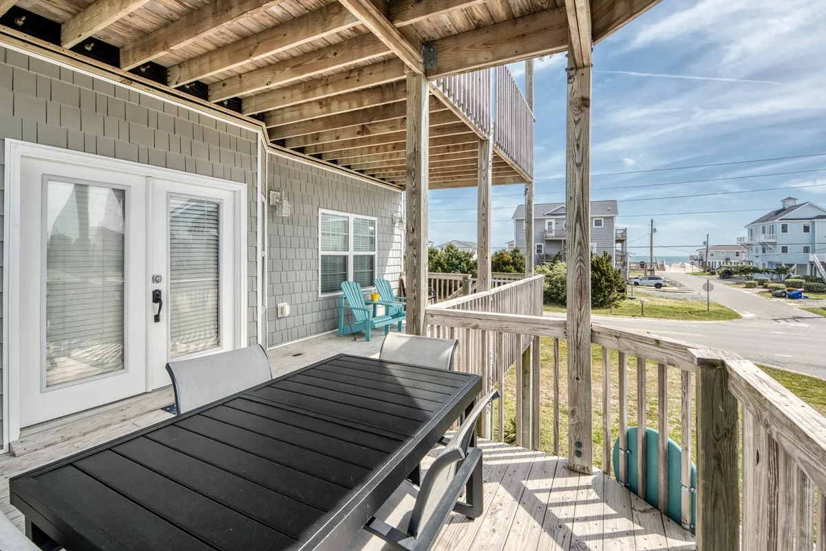 An exterior shot of the entry porch featuring an outdoor dining table with blue chairs, set against a beautiful ocean view. The inviting scene suggests moments of relaxation and social gatherings.