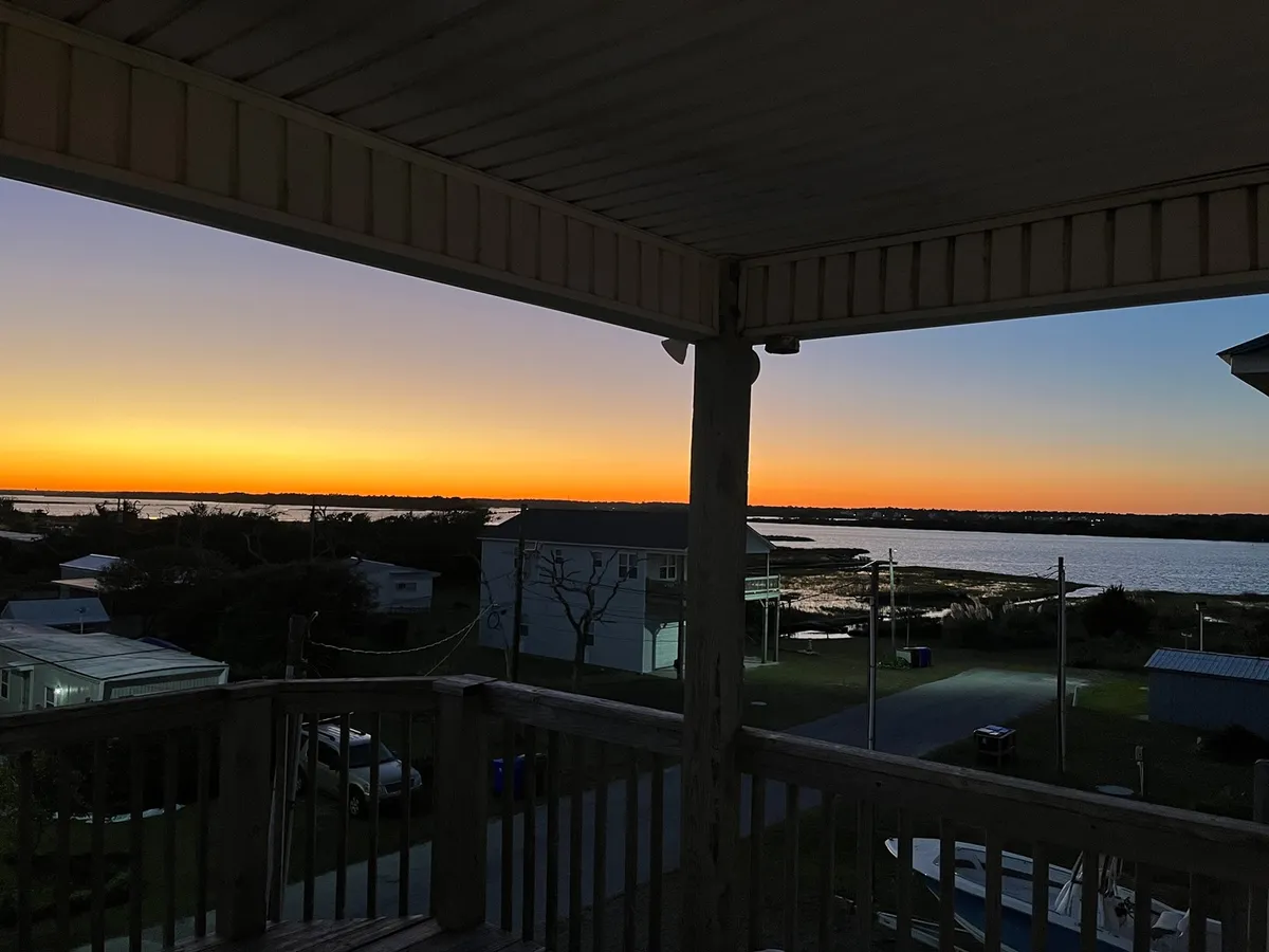 A serene sunset view over the sound, with the sky painted in warm hues and reflections dancing on the water. Silhouetted buildings hint at the nearby porch where families can unwind and soak in the evening rituals.