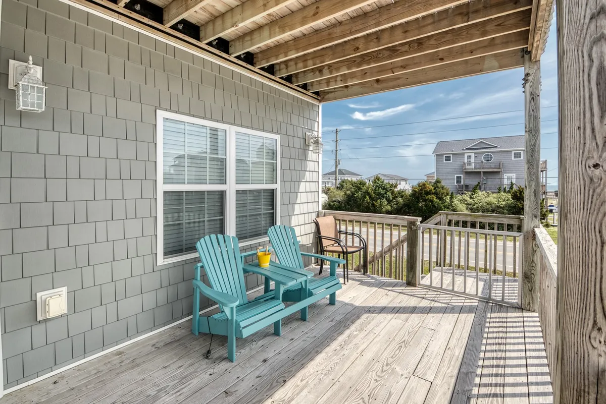 A cozy wooden deck is furnished with colorful Adirondack chairs and a planter with bright yellow flowers. The inviting setup is perfect for relaxing after a day at the beach, offering a tranquil spot to enjoy the outdoors with your dog at your side.
