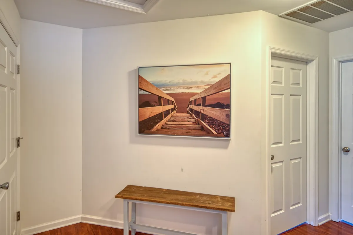 A bright and welcoming entryway featuring a wooden bench, framed landscape photo, and doors opening to the interior. The scene suggests a friendly and approachable atmosphere, ideal for greeting guests and sharing stories as people arrive at the property.