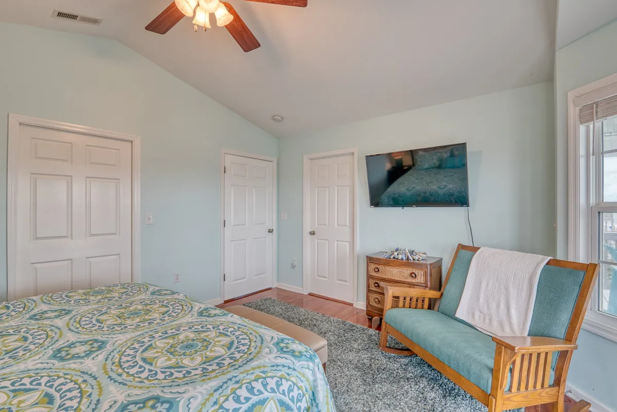 A bright bedroom with colorful bedding, a wooden chair, a dresser, and a wall-mounted TV. Sunlight streams into the room, creating a comfortable and serene atmosphere ideal for relaxation and privacy.