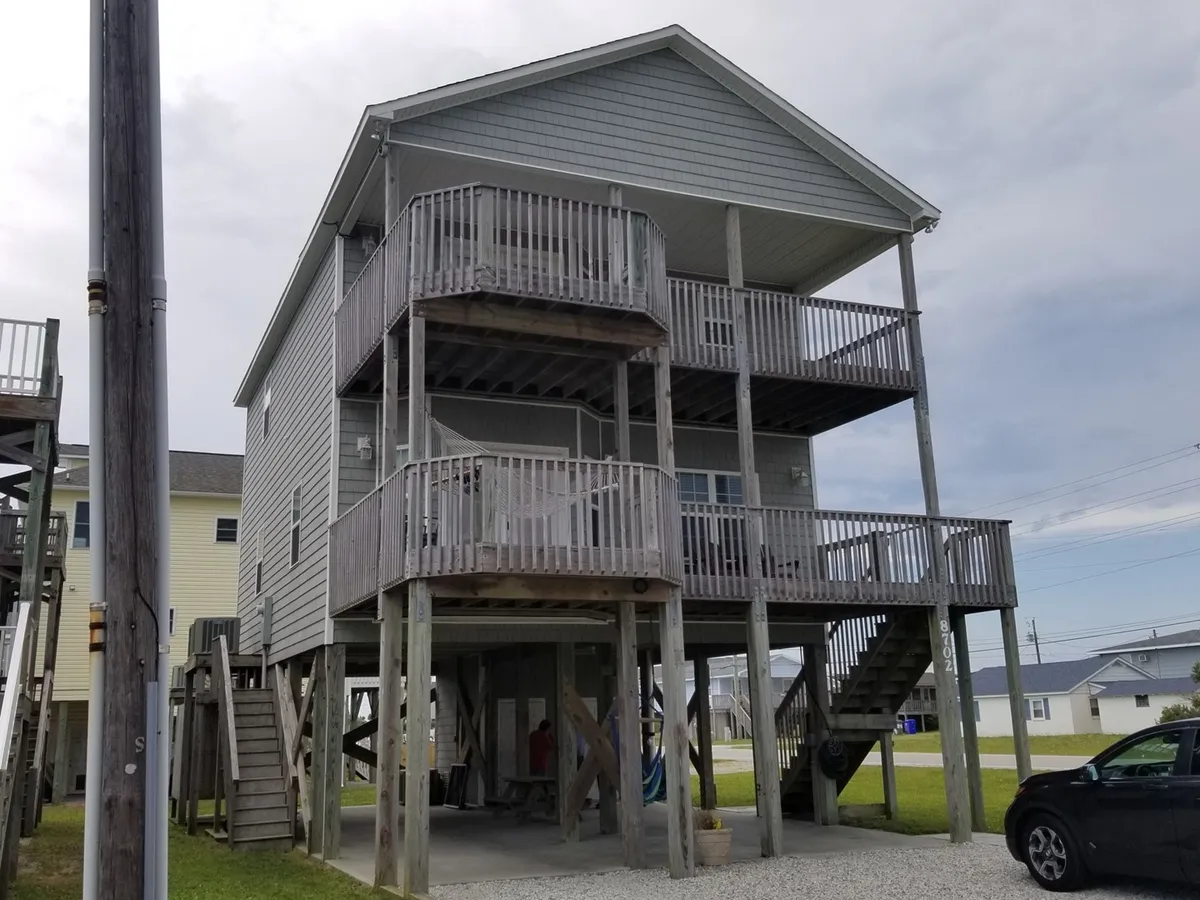 This exterior shot highlights the home's two balconies, wooden structure, and stilted foundation. The spacious balconies provide clear gathering spaces outdoors, while the building's design hints at multiple levels, which can be associated with accessibility features like an elevator.
