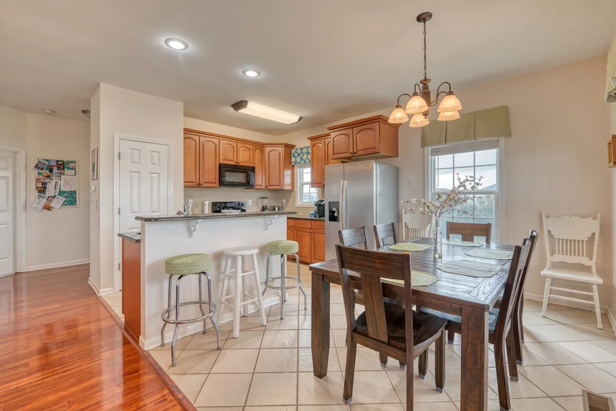 A warm, inviting dining and kitchen space with a central table, bar stools, and a window. The scene exudes a welcoming vibe, suggesting shared meals and casual gatherings.