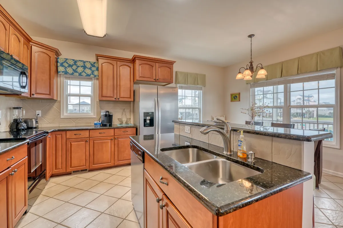 A modern kitchen with a central island, stainless steel appliances, wooden cabinetry, and plenty of natural light from the windows. The kitchen is designed for cooking, entertaining, and casual family dining.