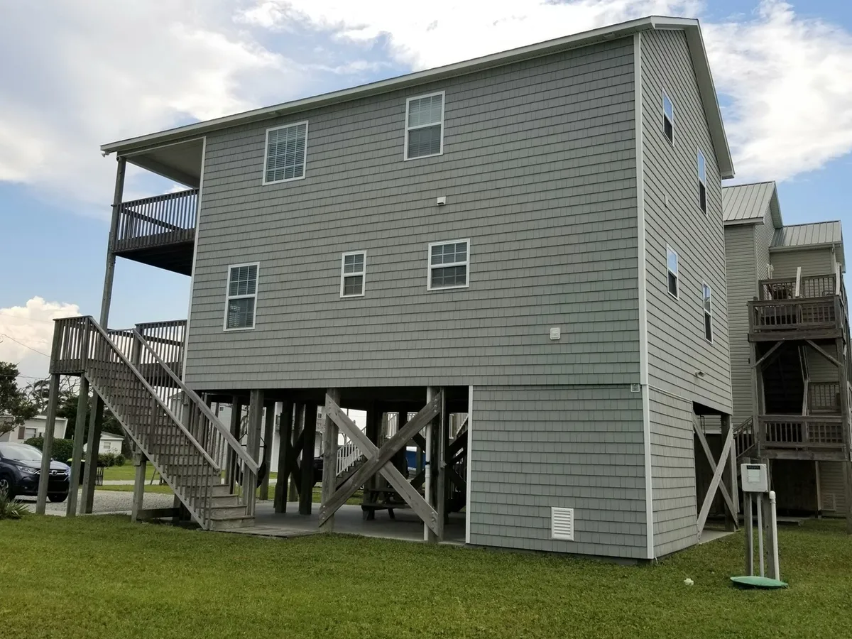 An exterior shot of the home featuring a multi-level structure with balconies overlooking a grassy yard, a staircase leading to the entrance, and inviting outdoor spaces. The yard below is perfect for family playtime or relaxing evenings.