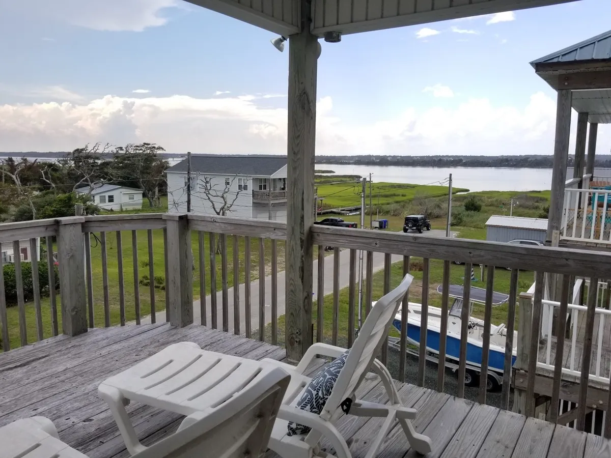This exterior scene shows deck chairs facing a tranquil water view, with distant houses visible. The arrangement encourages relaxation, shared moments, and enjoying sunsets together—activities mentioned in the section narrative.