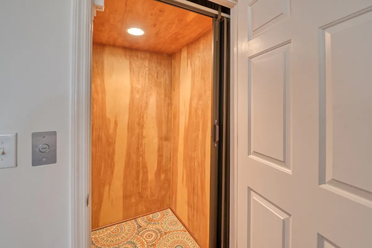 A view of the interior elevator, with wood paneling and decorative floor tiles, emphasizing smooth transitions between floors. The elevator is easily accessible from the ground level, making it suitable for all family members including those with strollers or mobility needs.