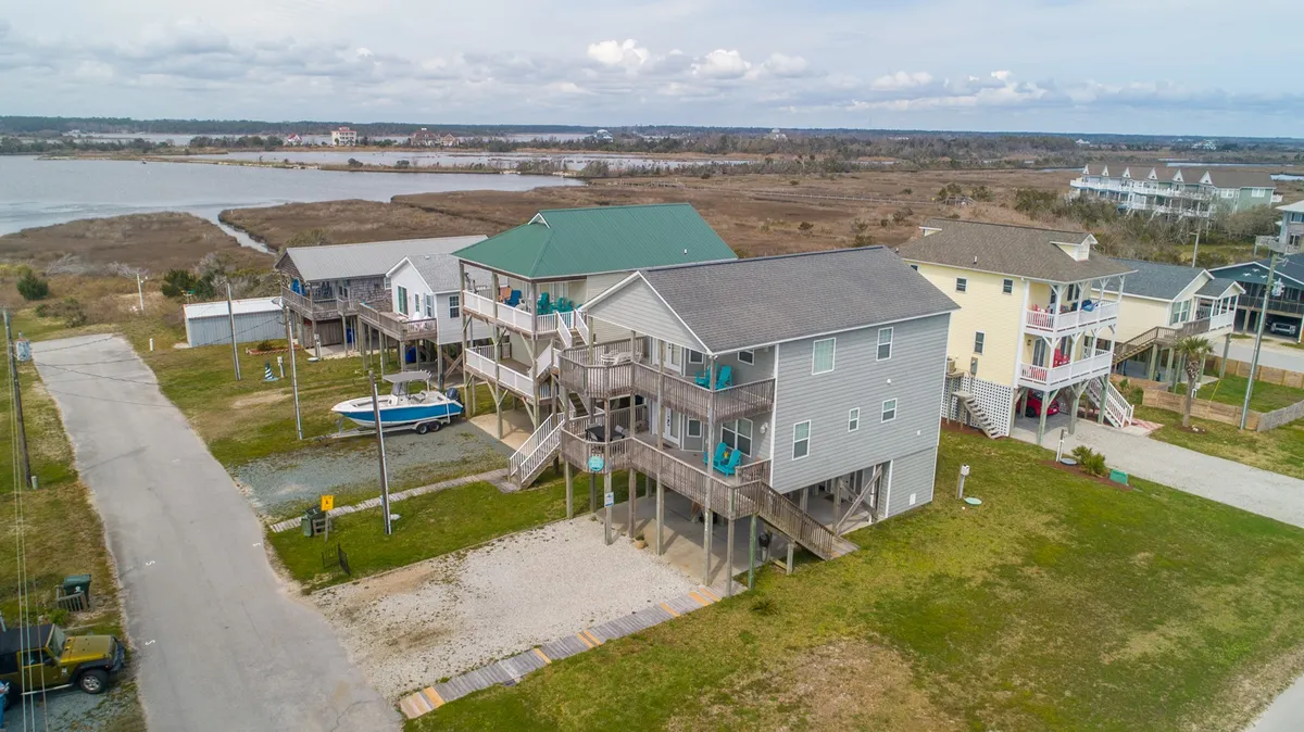 A broad exterior view captures multi-level houses with green roofs, nestled among the landscape with a waterway in the background. The spacious setting suggests ample parking and space, welcoming extended family or larger groups.